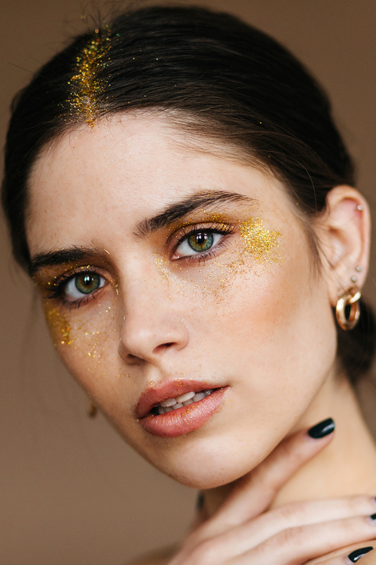 Lovable european girl with golden eyeshadows looking to camera. Close-up photo of blithesome brunette woman isolated on brown background.